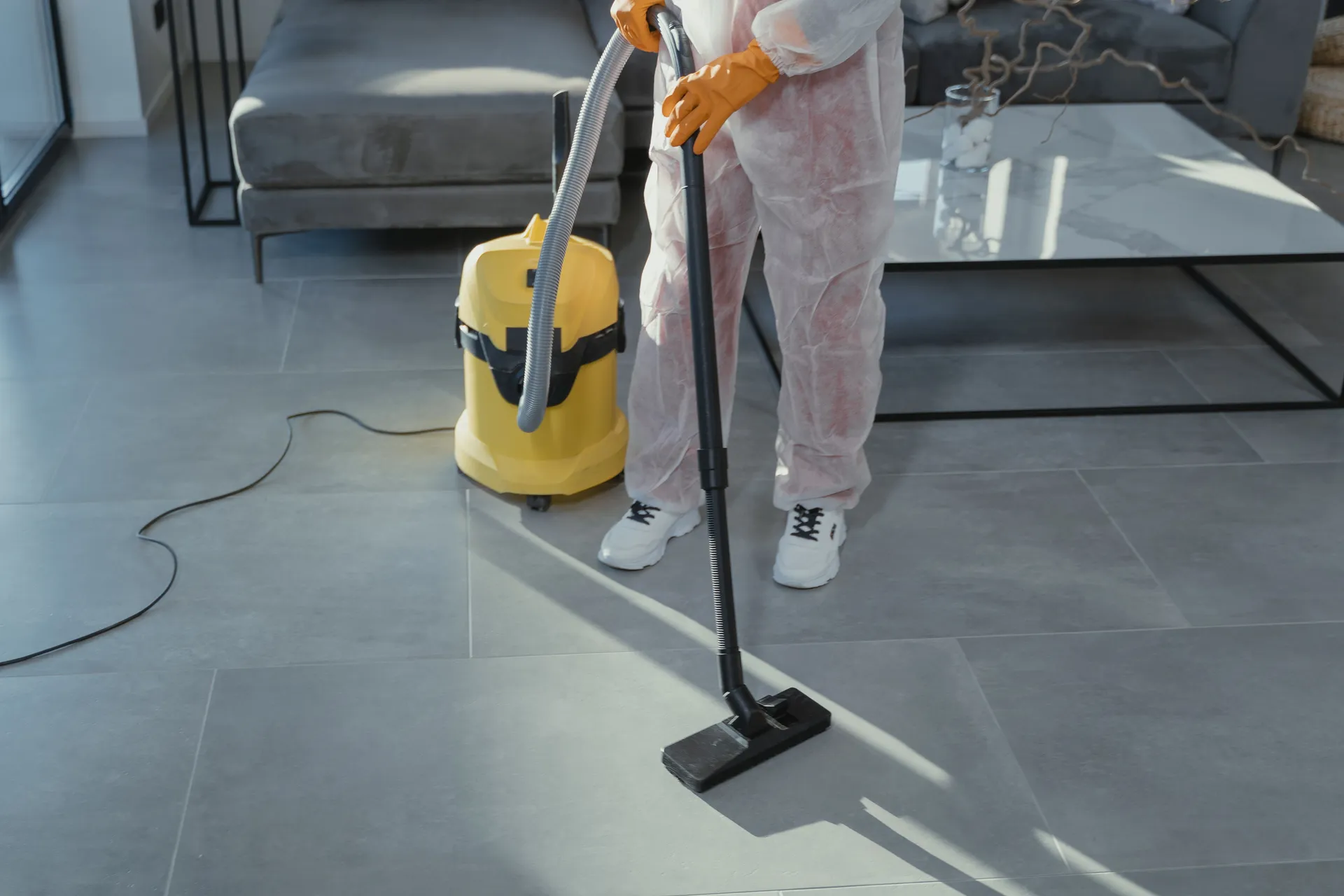 A cleaner vacuuming a modern living room floor with a wet/dry vacuum