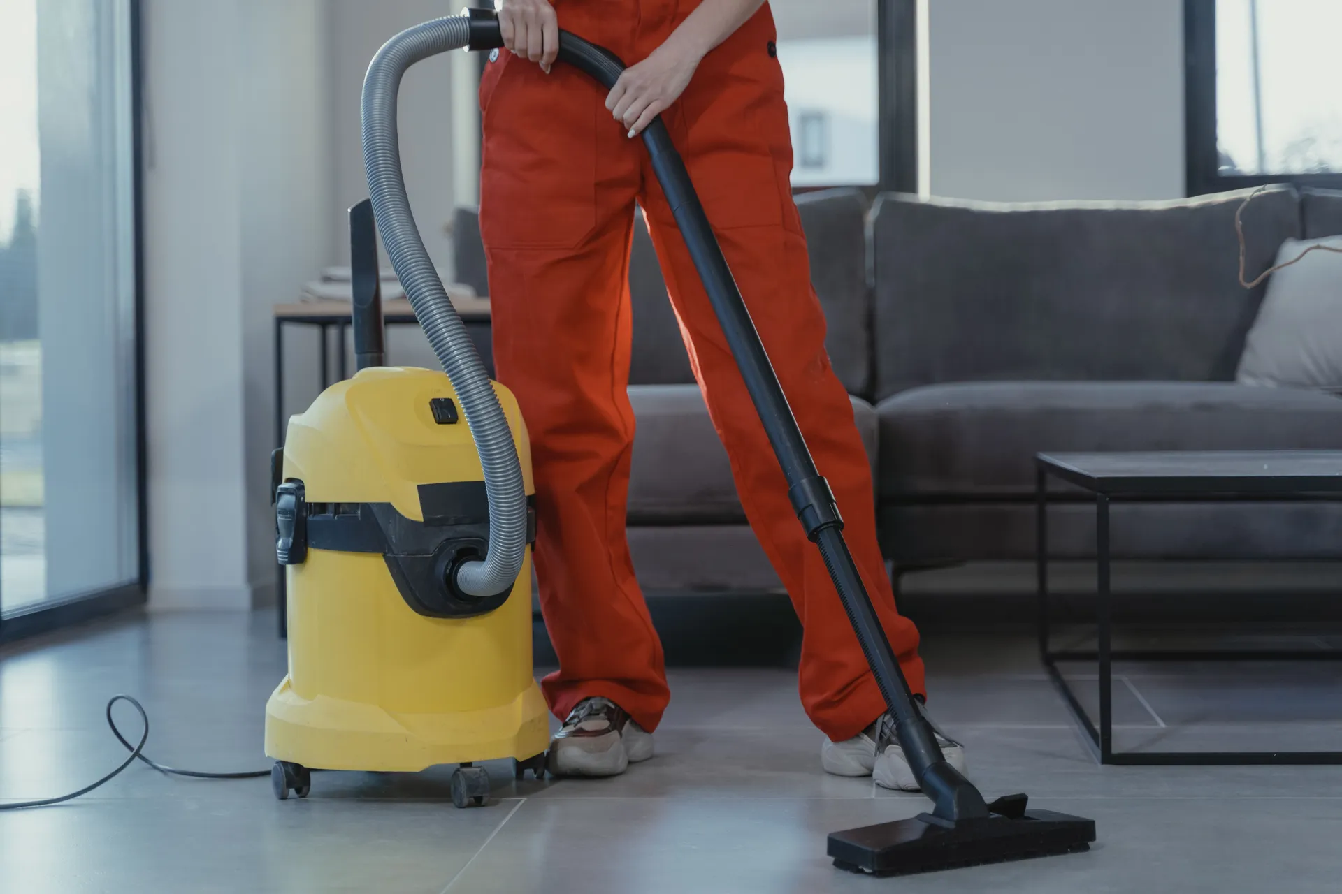 A cleaner vacuuming a modern living room floor with a wet/dry vacuum